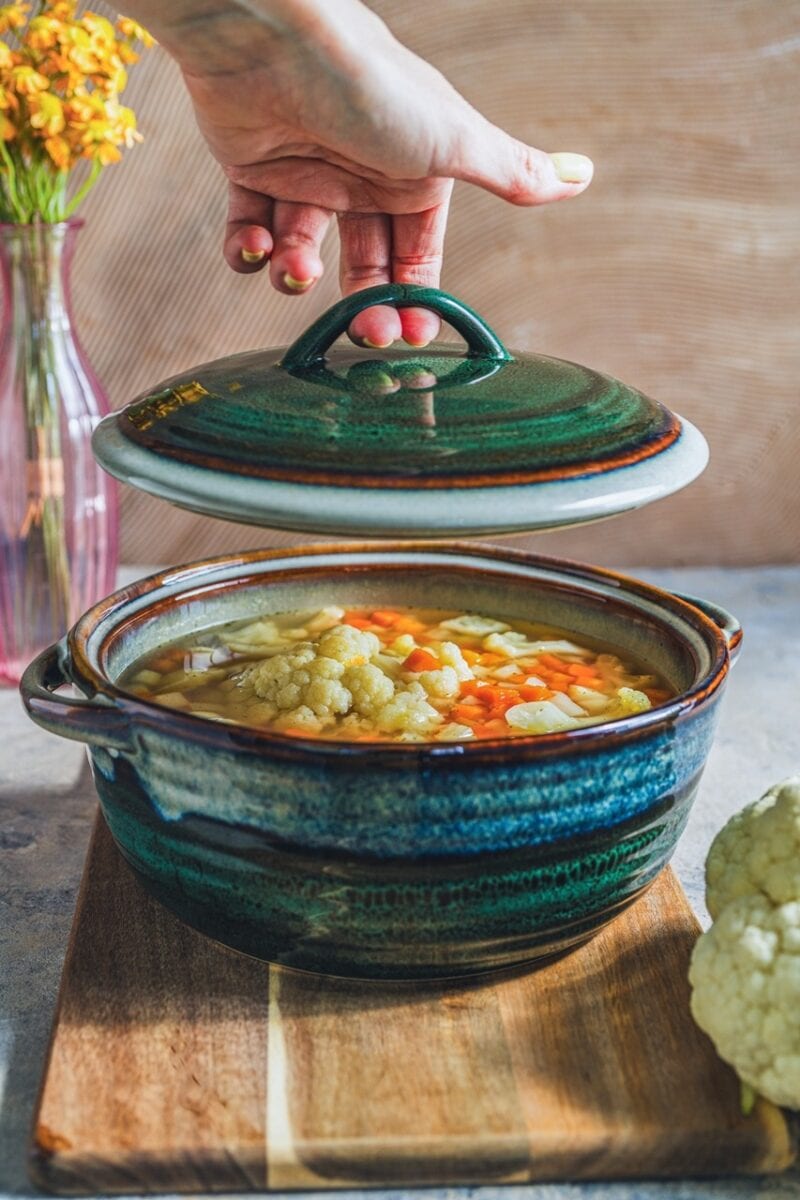 Szklany kapturek na ceramicznej garnku z warzywami, idealny do domowych zup i gulaszy, elegancki design, ręczna ceramika, rustykalny klimat kuchni, funkcjonalne naczynie do gotowania i podawania potraw.