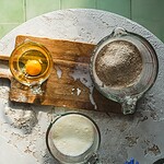 Jajko, mąka i mleko na białym stole, przygotowania do domowego wypieku, naturalne składniki, zdrowe jedzenie, śniadanie, kuchnia domowa, wegetariańskie przepisy, gotowanie, domowe wypieki, otoczenie zielonych płytek.