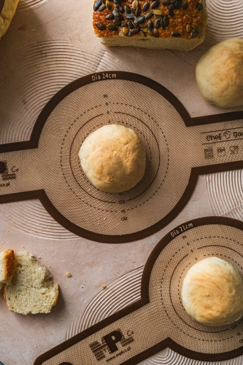 Miękkie ciasto na bazie naturalnych składników, gotowe do pieczenia, na stole kuchennym z funkcjonalną matą do wyrabiania i formowania wypieków, idealne do pieczenia chleba i bułek.